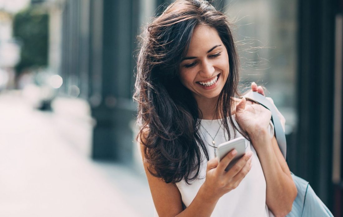 Junge Frau hält ihr Handy in der Hand und lächelt